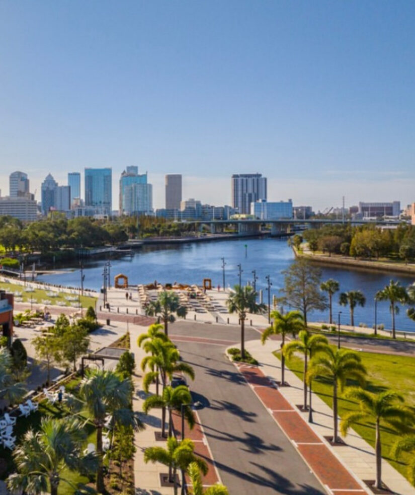 A sunny view of downtown Tampa’s skyline, the river, palm trees, Armature Works, and the Westshore Grand Hotel in the vibrant city foreground.