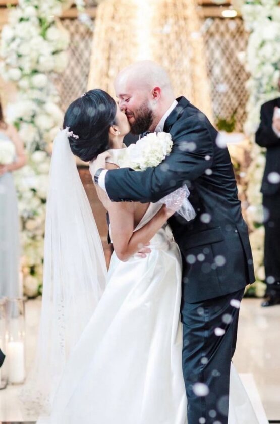 A bride and groom kiss at their Westshore Grand Hotel wedding ceremony, surrounded by flowers and applauding guests.