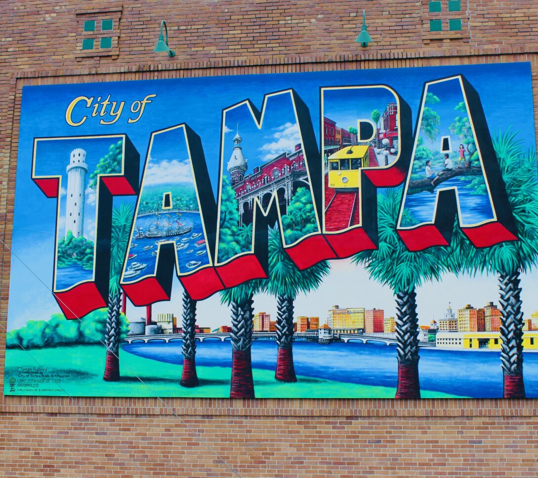 A mural reads City of Tampa with Tampa landmarks inside large, colorful block letters, bordered by palm trees and a blue sky.