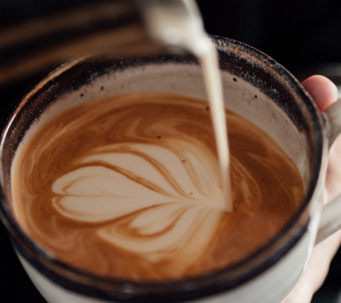 A close-up of milk being poured into a cup of coffee with a heart-shaped latte art design on top.