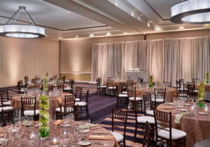 Elegant banquet hall with round tables, brown chairs, floral centerpieces, and draped backdrop, ready for an event.